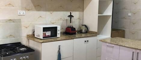 A kitchen with white cabinets, a microwave, a gas stove, and a kettle.