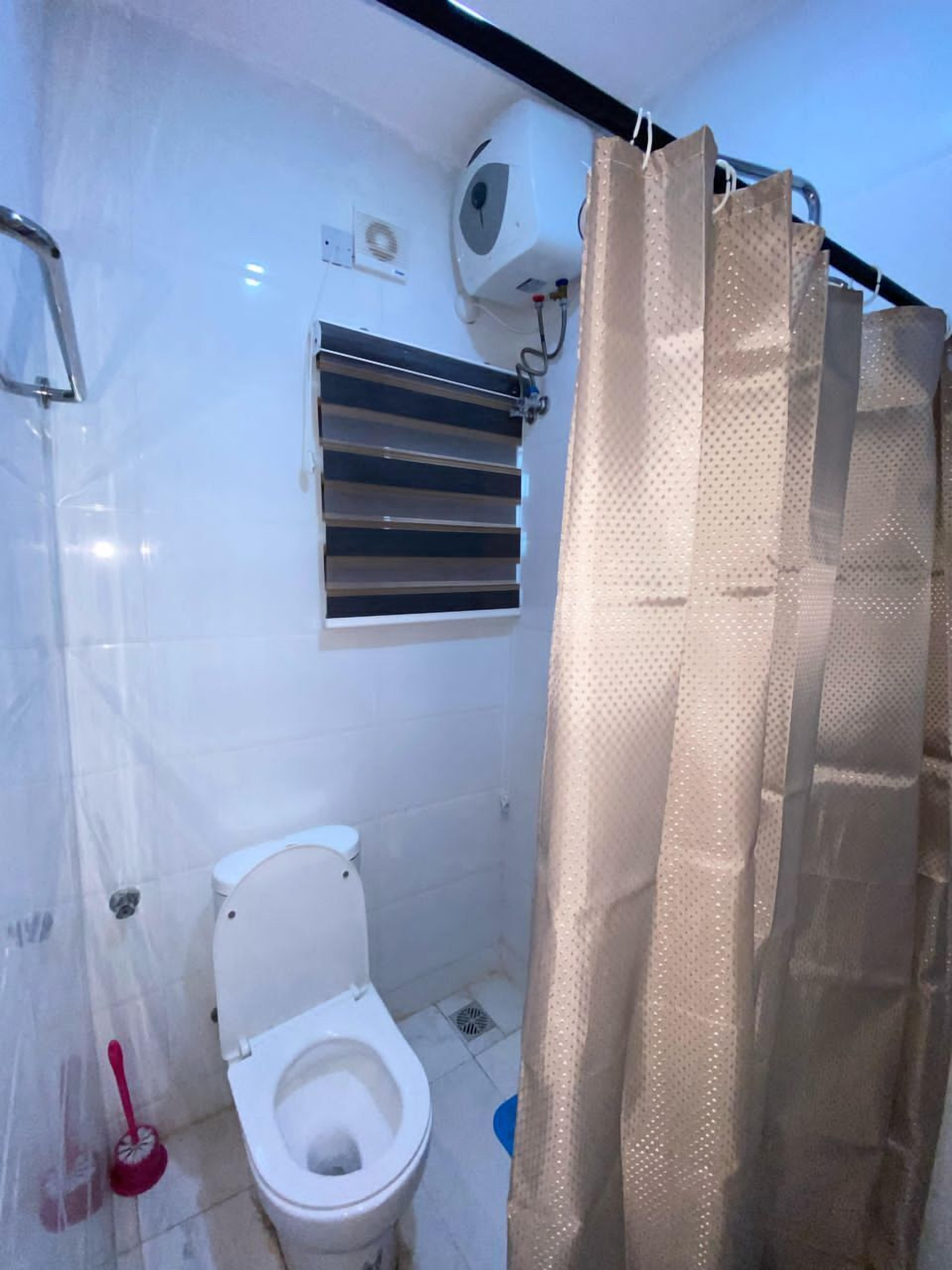 Un baño con inodoro, cortina de ducha y ventana con persianas.
