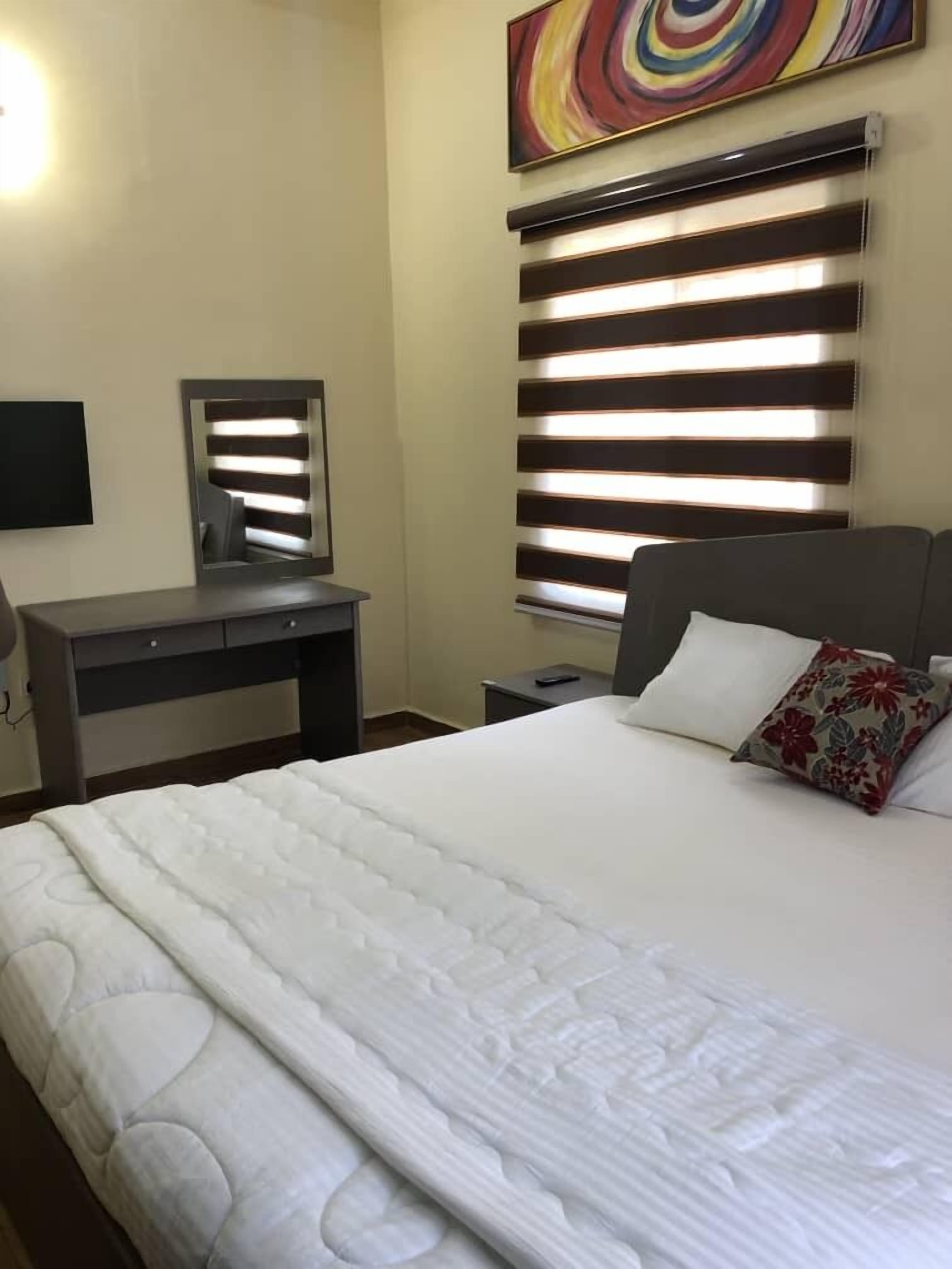 A hotel room with a bed, a desk, a mirror, and a wall-mounted TV.
