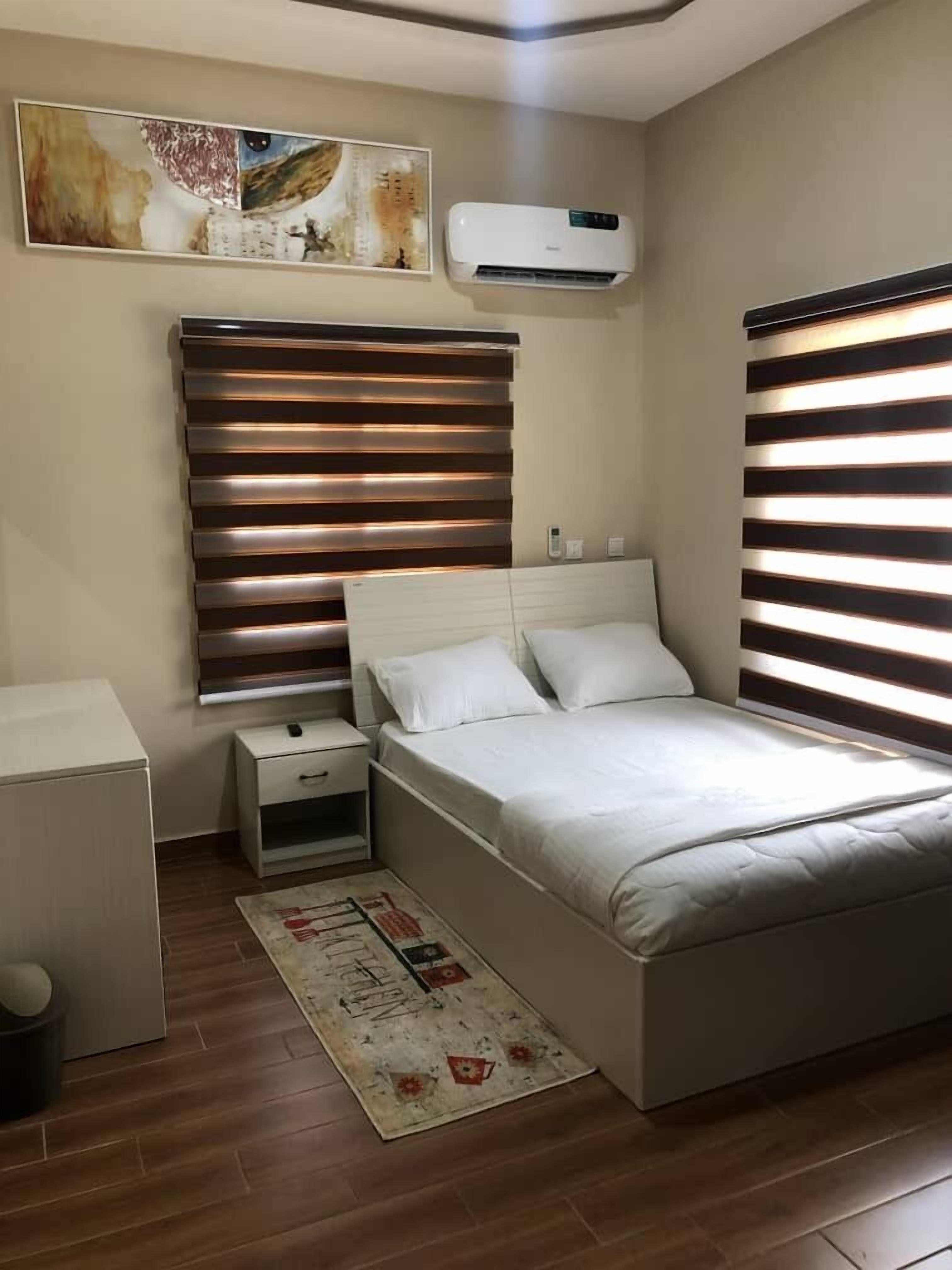 A bedroom with a bed, bedside tables, an air conditioner, and a painting on the wall.