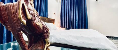 Una habitación con una cama, una estatua, un control remoto y cortinas azules.
