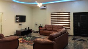 A modern living room with a flat-screen TV, leather sofa, and a patterned rug. - Hilton Summer Apartments (Abuja)
