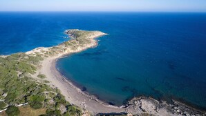 An aerial view of a coastal area with a beach, clear blue waters, and rocky terrain.