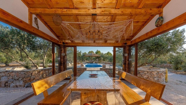 A covered outdoor dining area with wooden benches and a table, overlooking a pool and trees. - Eco Villa Solus with two pools (Drage)