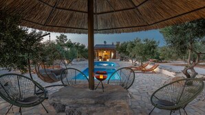 A stone patio with a pool, lounge chairs, and a thatched umbrella. - Eco Villa Solus with two pools (Drage)