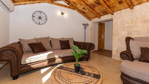 A cozy living room with a wooden ceiling, a round coffee table with a plant, a brown sofa, and a stone wall. - Eco Villa Solus with two pools (Drage)