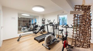 Een sportschool met diverse fitnessapparaten, een spiegel en een bordje dat een sportlounge aangeeft.