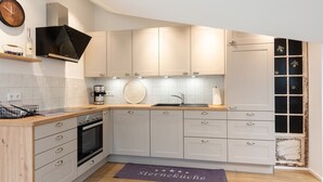 A modern kitchen with white cabinets, a built-in oven, a coffee maker, and a decorative backsplash. - Ferienwohnung Sternenhimmel mit Bergblick, 2 Separate Schlafzimmer, Wlan (Rottau)