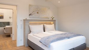 A modern bedroom with a bed, a headboard, a painting, and a bathroom visible in the background. - Ferienwohnung Sternenhimmel mit Bergblick, 2 Separate Schlafzimmer, Wlan (Rottau)