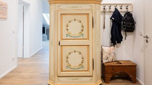 A hallway with a wooden cabinet featuring floral designs, a coat rack with jackets, and a small wooden bench. - Ferienwohnung Sternenhimmel mit Bergblick, 2 Separate Schlafzimmer, Wlan (Rottau)