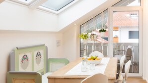 A dining area with a wooden table, chairs, a glass-top table, and a view of a balcony with plants and a railing. - Ferienwohnung Sternenhimmel mit Bergblick, 2 Separate Schlafzimmer, Wlan (Rottau)