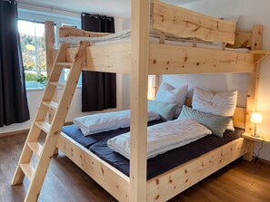 A bunk bed with a wooden ladder, multiple pillows, and a bedside table with a lamp.