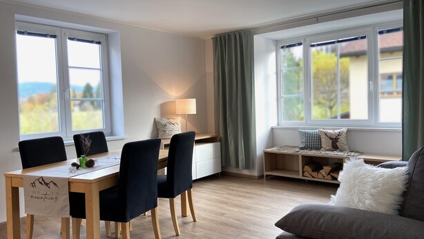 A modern living room with a dining area, large windows, and a cozy seating area. - Großzügige Ferienwohnung zum Entspannen und Wohlfühlen, 78 m², 4 Personen, Wlan (Siegsdorf)