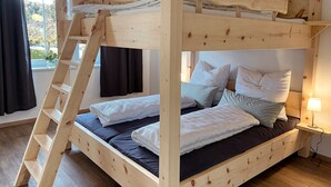 A bunk bed with a wooden ladder, a bedside table with a lamp, and a view of the outdoors through a window. - Großzügige Ferienwohnung zum Entspannen und Wohlfühlen, 78 m², 4 Personen, Wlan (Siegsdorf)