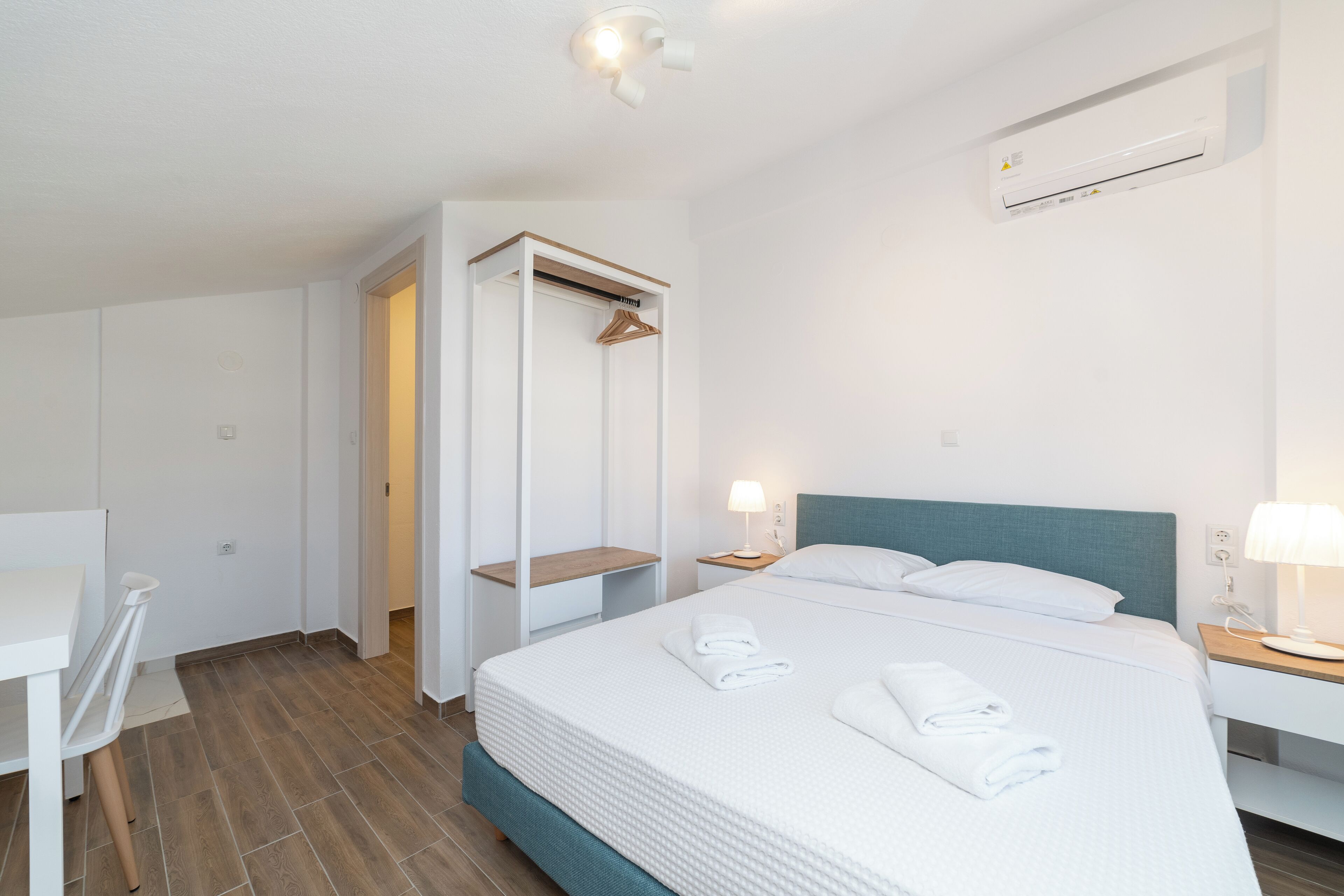 A hotel room with a bed, bedside tables, a wardrobe, and a desk.