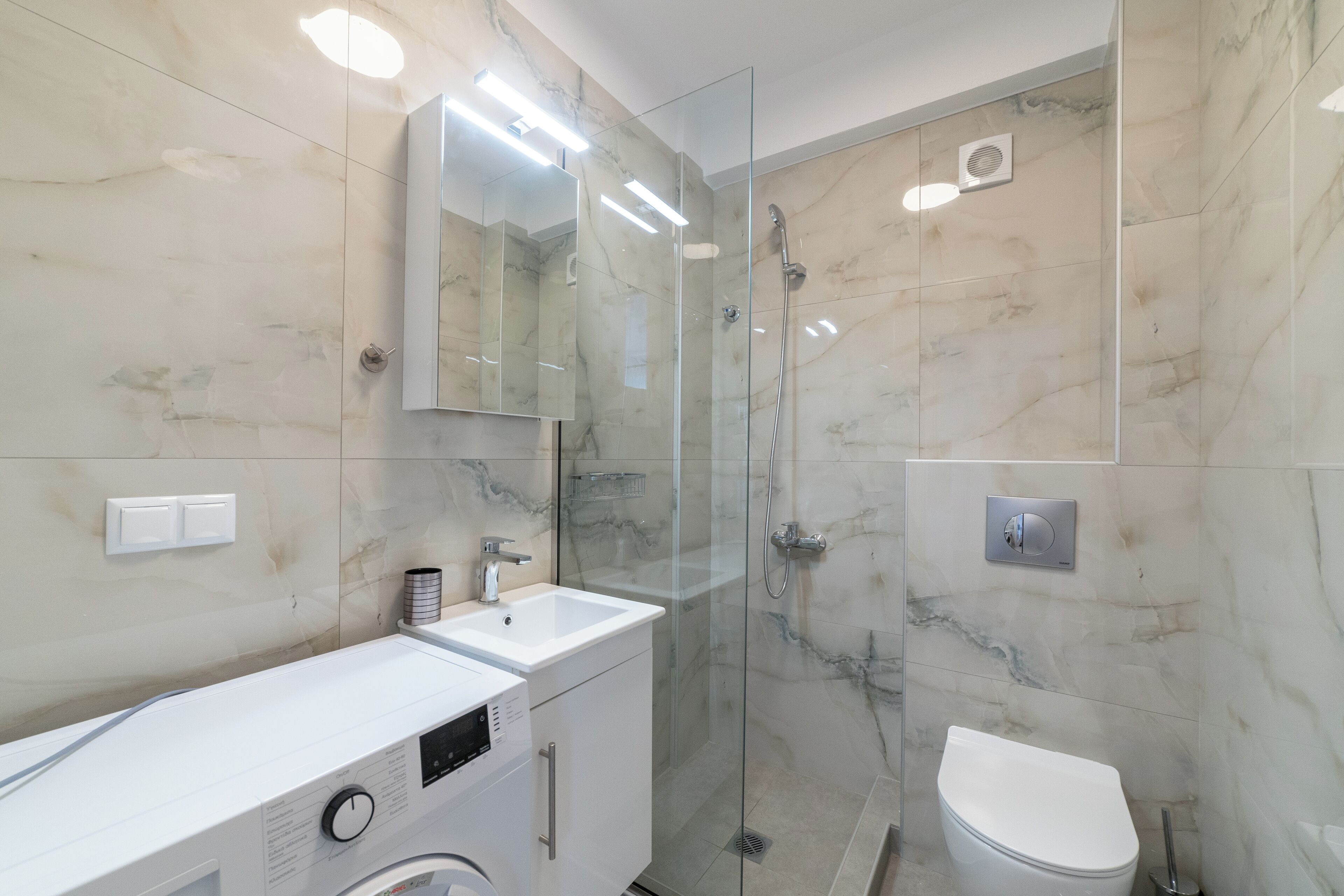 Un baño moderno con ducha envuelta en vidrio, un lavamanos blanco y un inodoro.