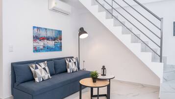 A modern living room with a blue sofa, a painting, a floor lamp, and a staircase.