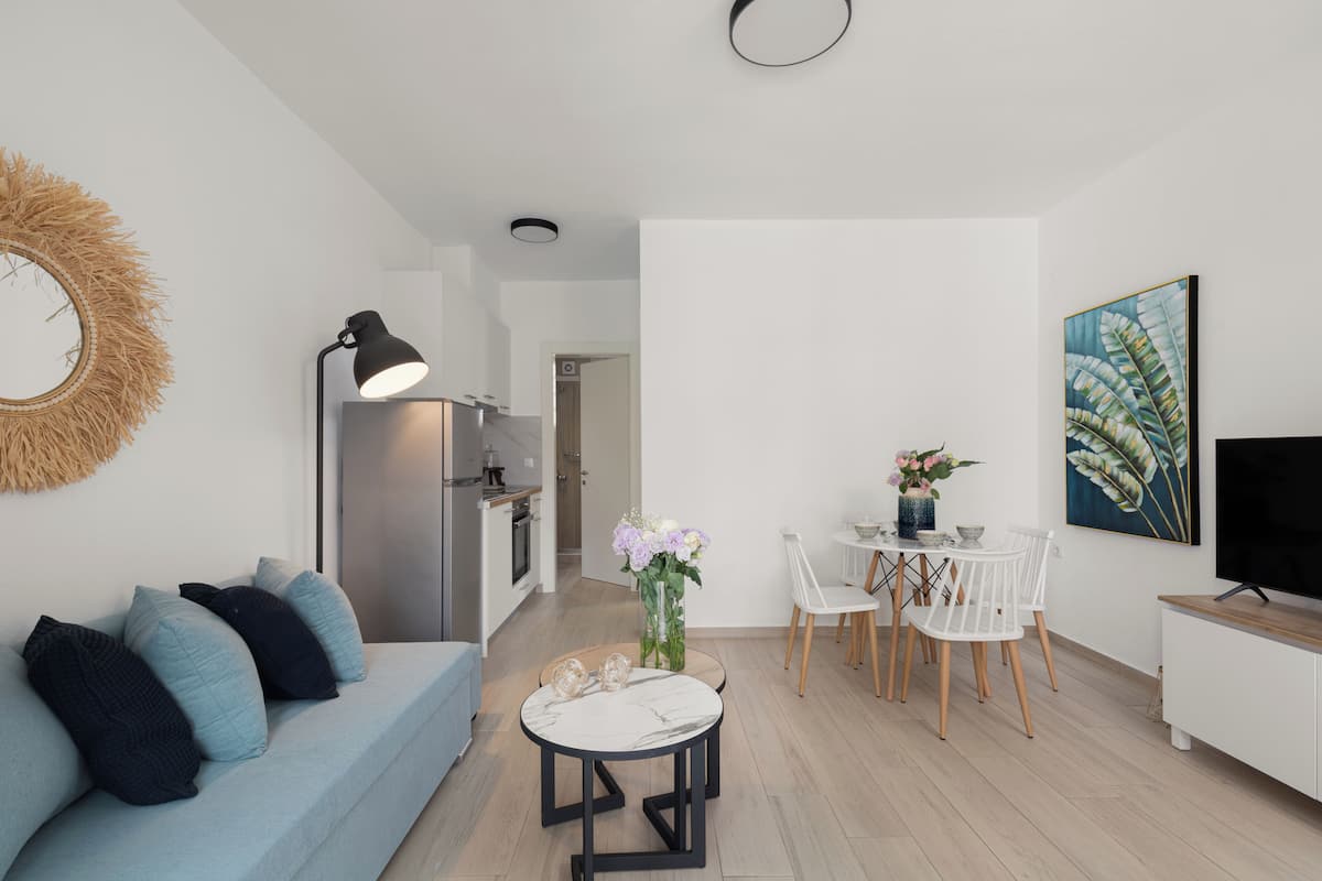 Een moderne woonkamer met een bank, een eettafel, stoelen, een televisie en een keukenhoek.