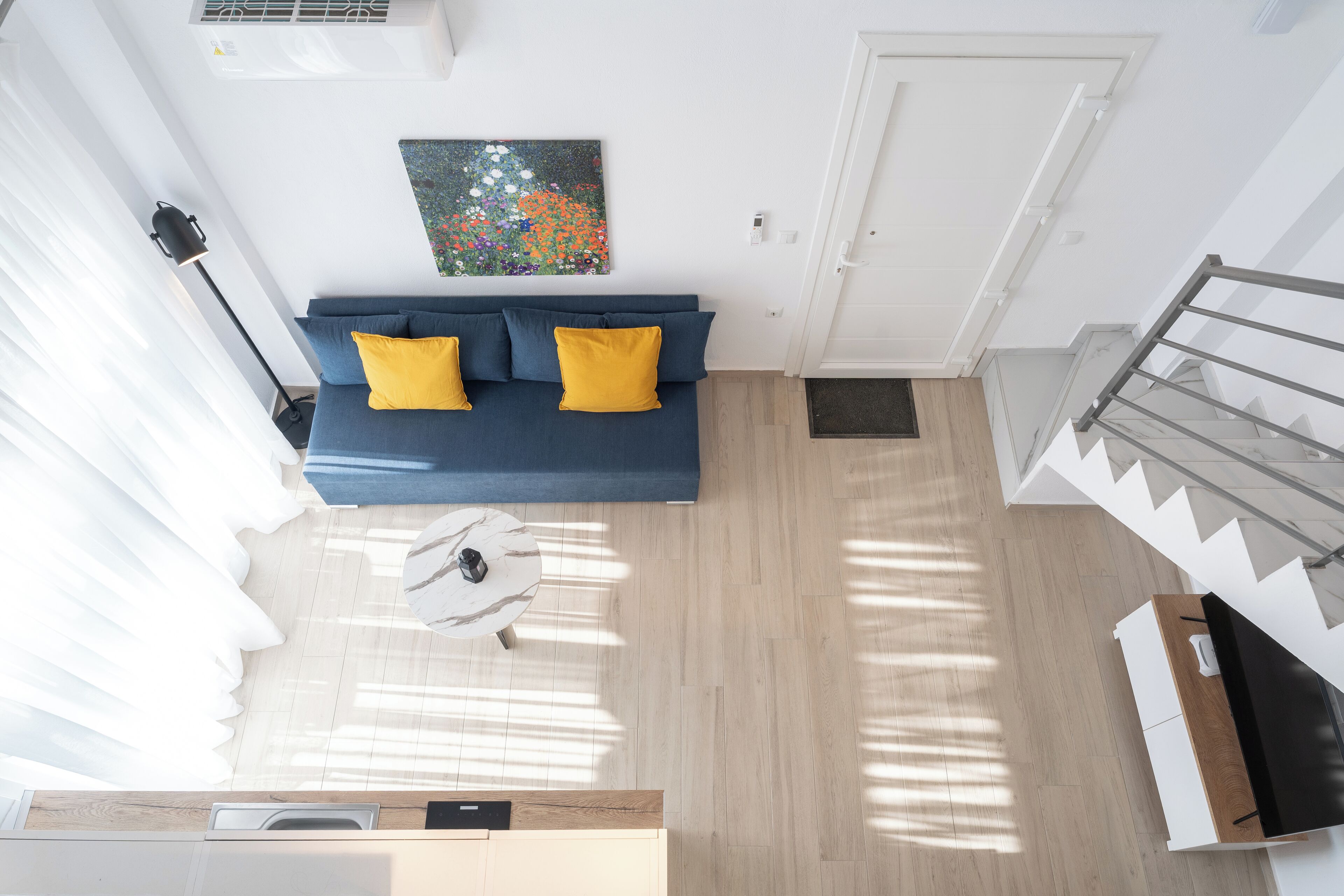 Un saló modern amb un sofà blau, una taula de centre rodona i una escala a la dreta.
