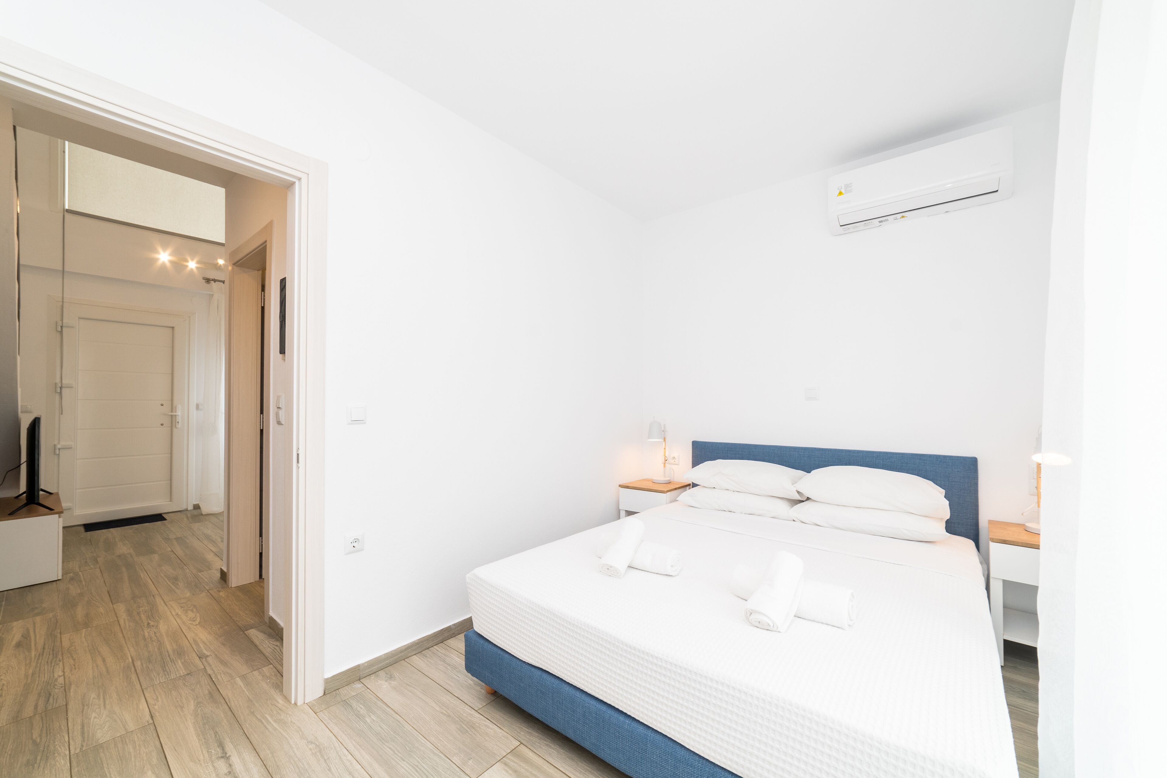 Habitación de hotel con cama, mesitas de noche, equipo de aire acondicionado y una puerta que da a otra habitación.