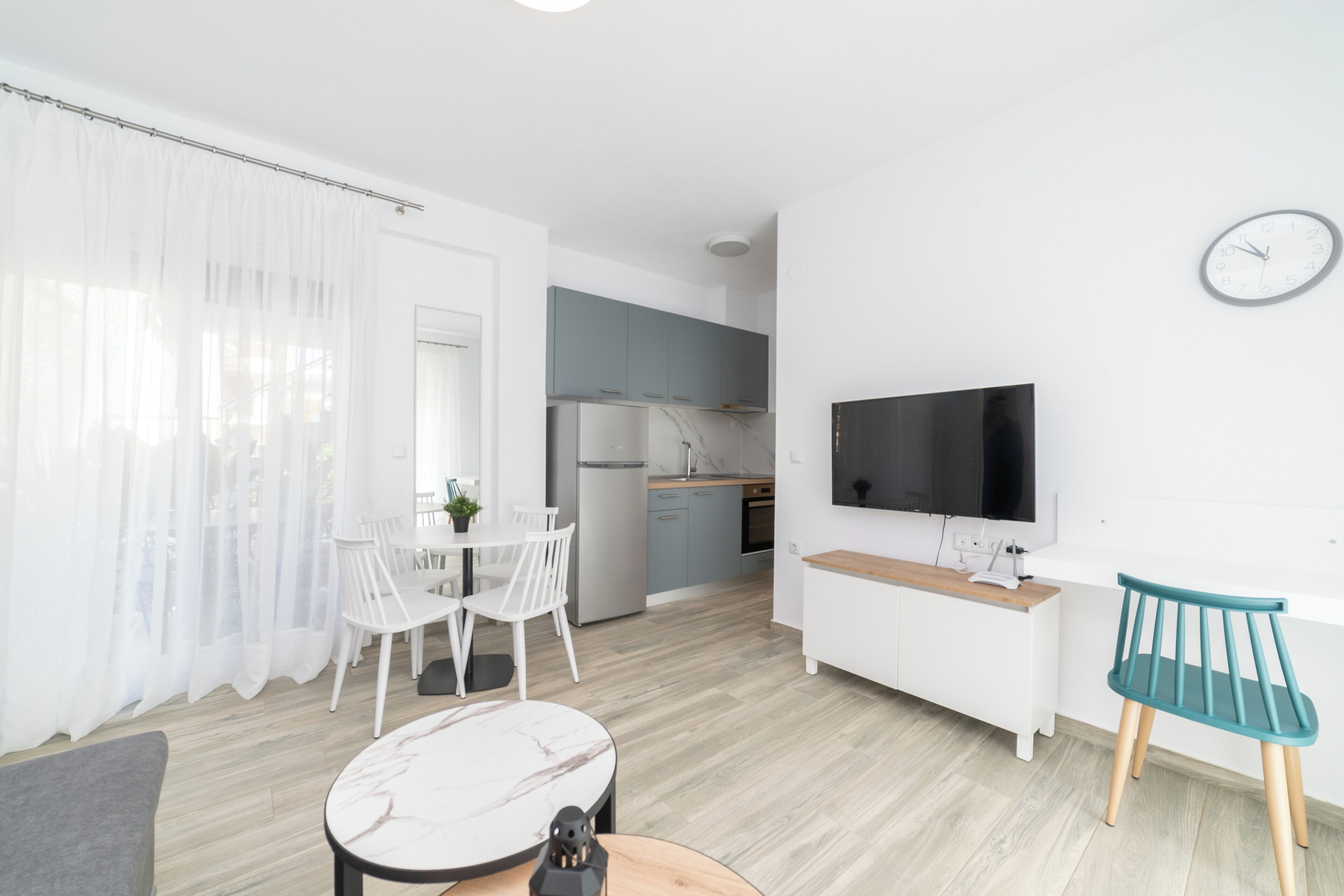 A modern, well-lit room with a dining area, a kitchen, and a TV.