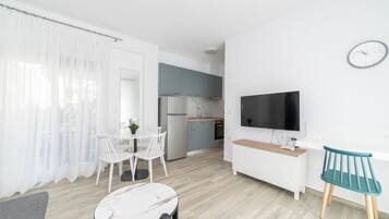 A modern, well-lit room with a dining area, a kitchen, and a TV.