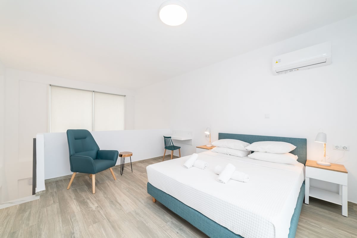 Een moderne hotelkamer met een groot bed, een stoel, een bureau en een airconditioning.