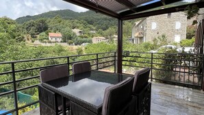 Ein überdachter Außenbereich mit Tisch und Stühlen, mit Blick auf eine malerische Hügellandschaft und Gebäude.