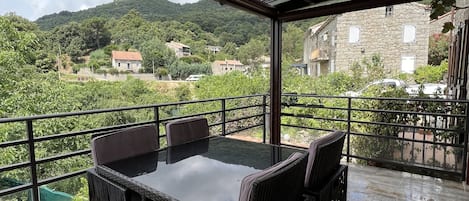 Un espacio de estar al aire libre cubierto, con una mesa y sillas, que ofrece vistas a una colina pintoresca con edificios.