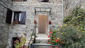 Ein Steinhaus mit einer Holztür, einer kleinen Veranda und Blumentöpfen.