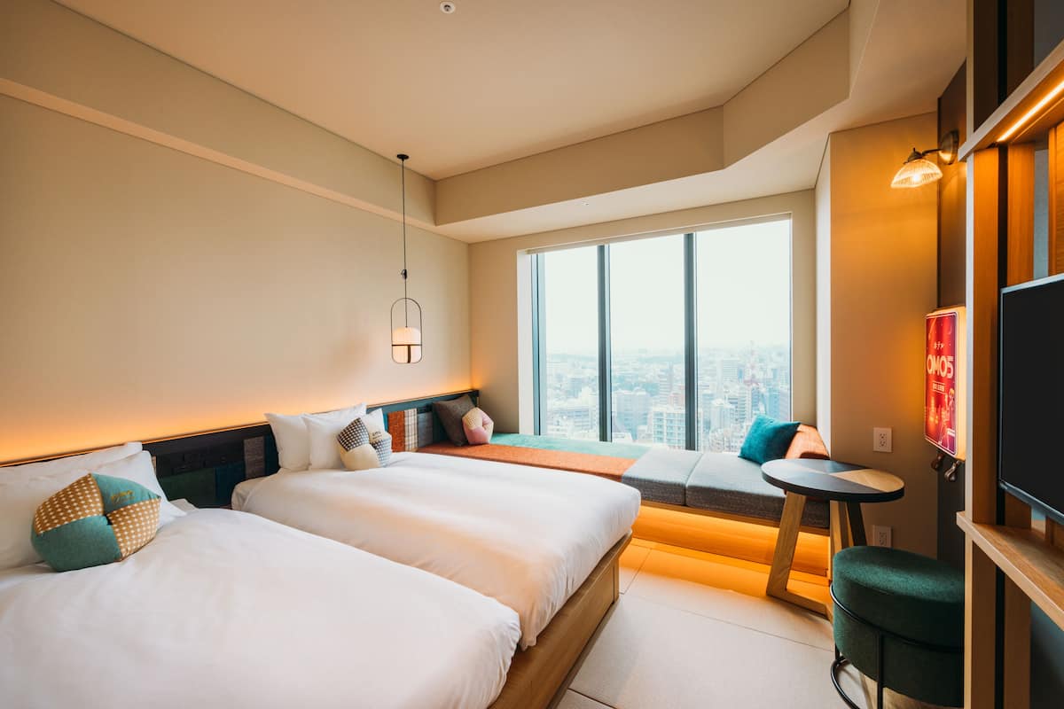 Une chambre d’hôtel moderne avec deux lits, un coin salon, une télévision et une vue sur la ville.