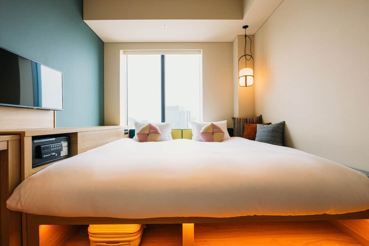 Une chambre d’hôtel avec un grand lit, une télévision, une fenêtre donnant sur la ville et une lampe de chevet.