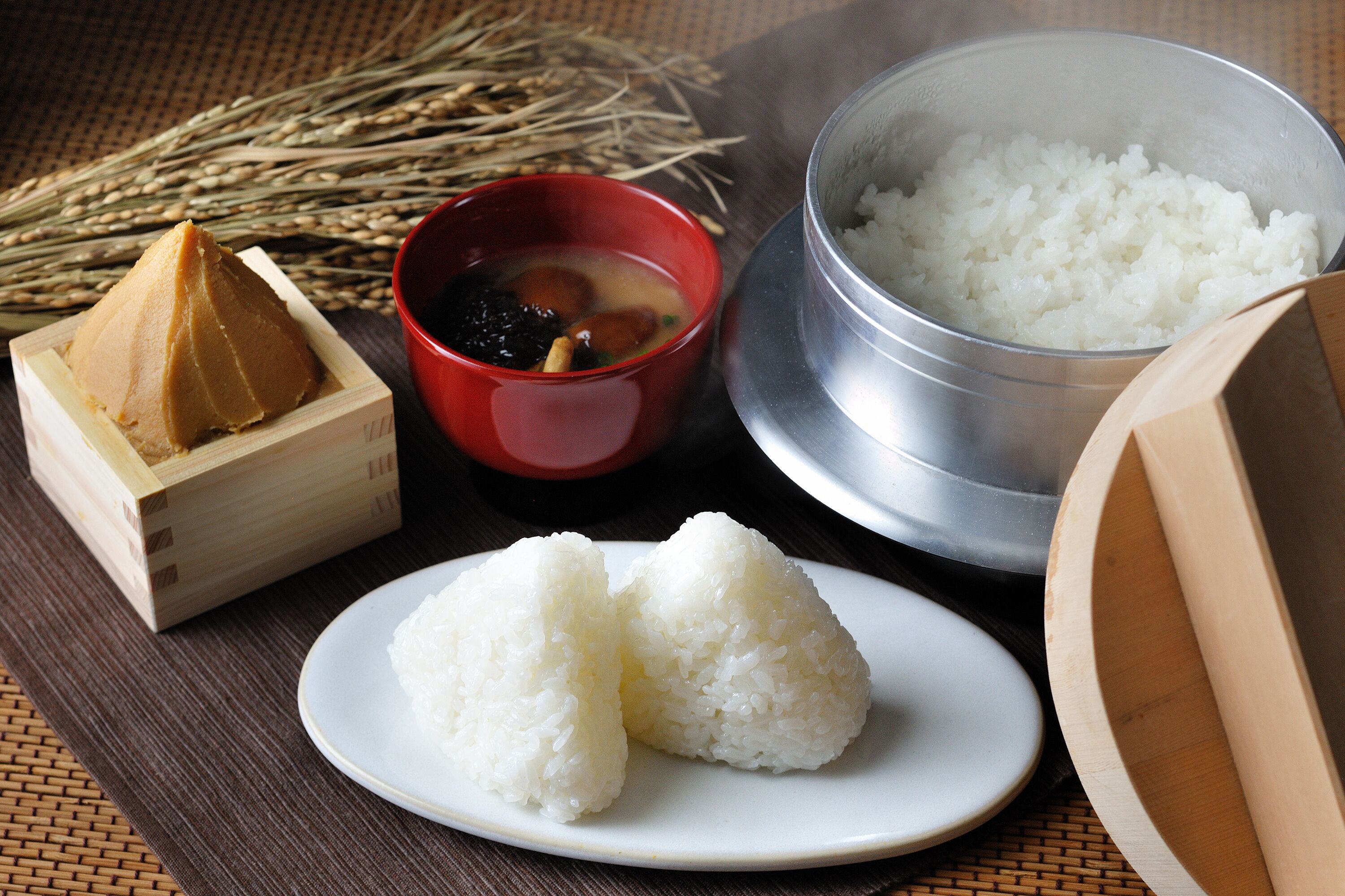 A wooden table with a bowl of white rice, a red bowl with a dark liquid, and a wooden box containing a brown substance.