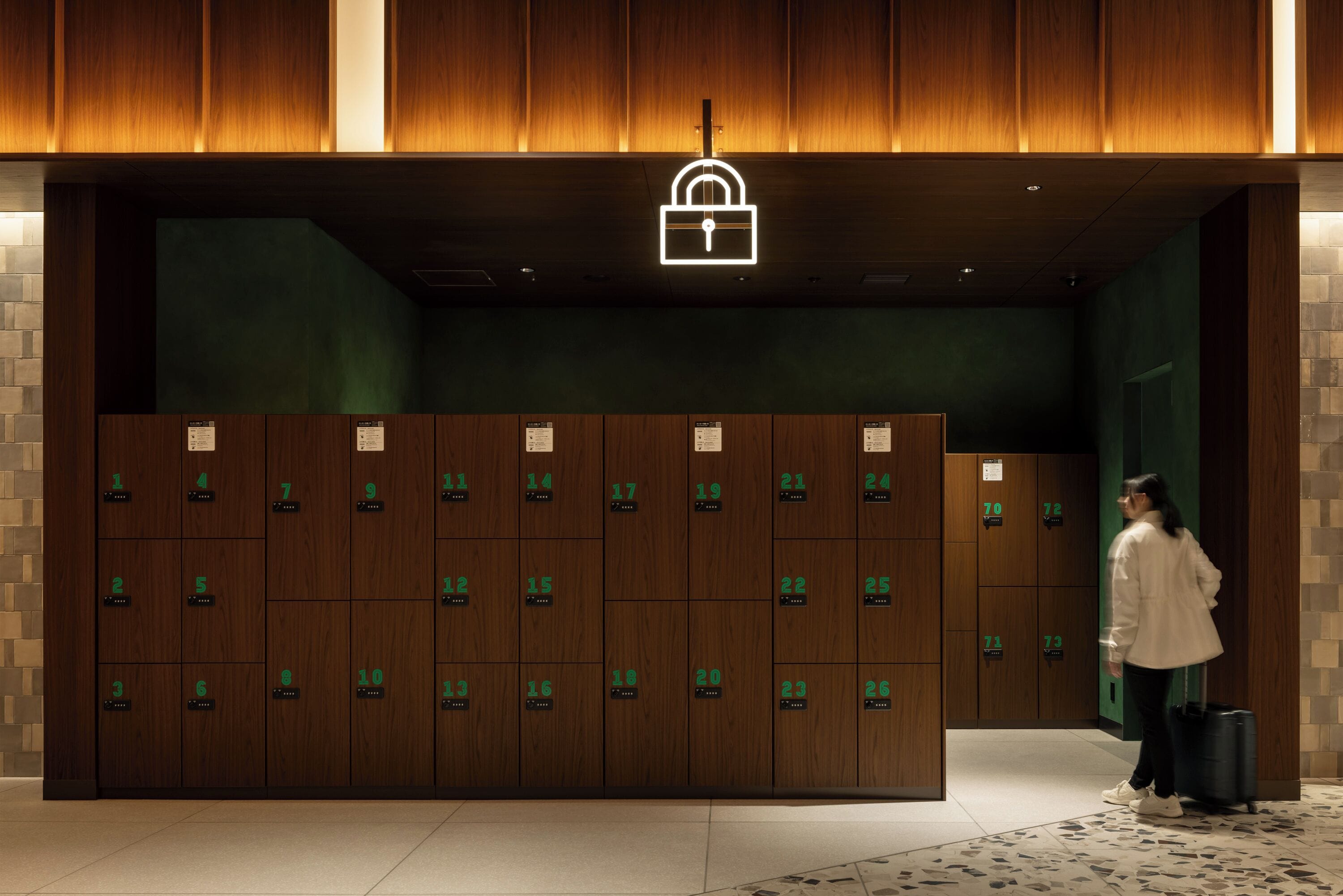 A row of wooden lockers with numbered tags, a lock symbol above, and a person with a suitcase.