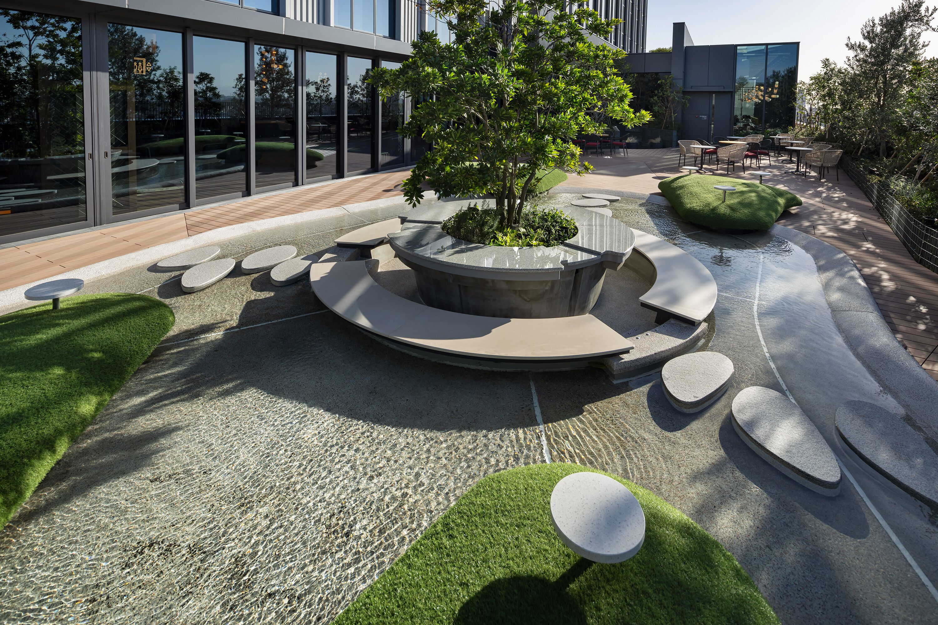 Un espace extérieur moderne doté d’un aménagement circulaire central, entouré de jardinières et d’un petit arbre.