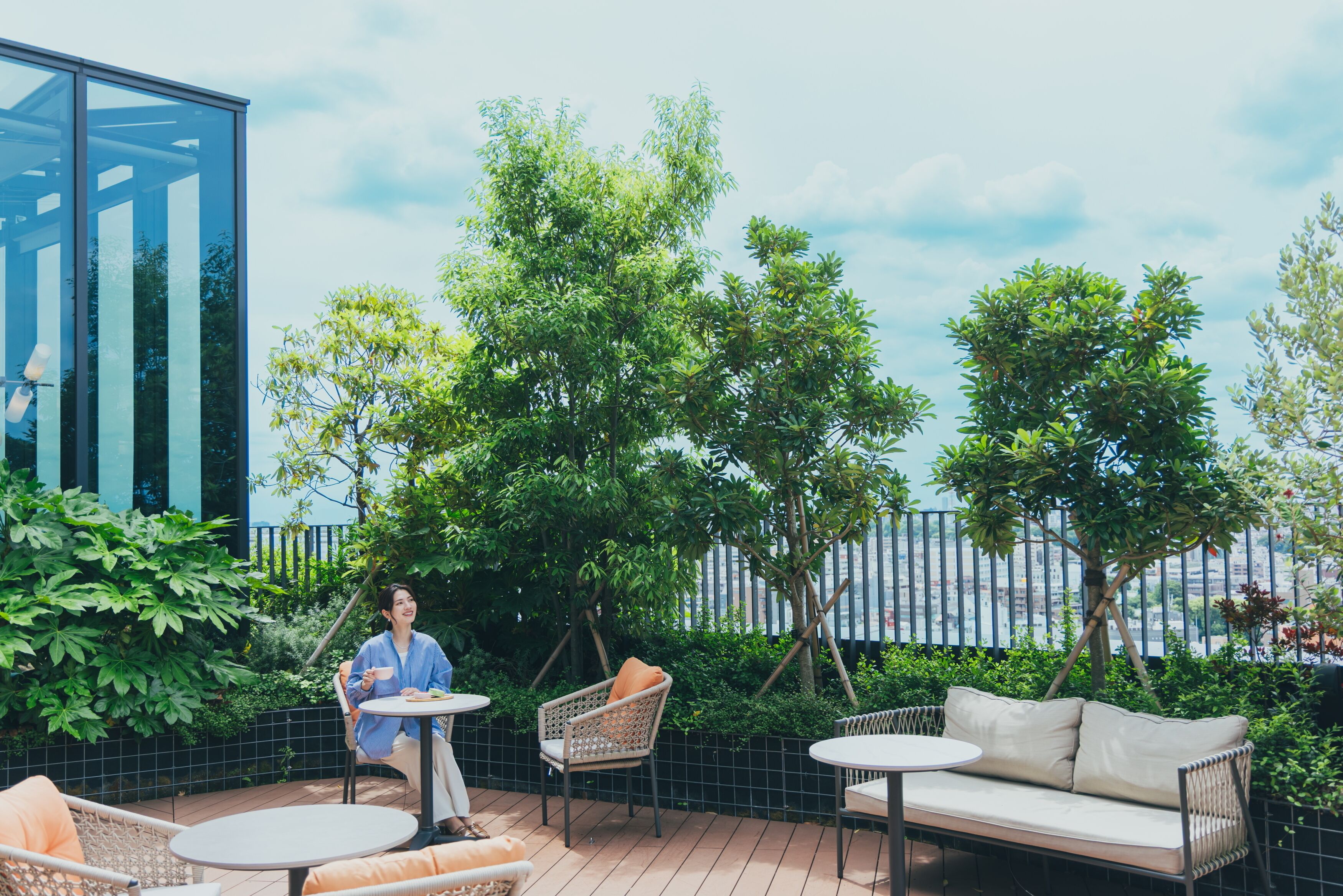 An outdoor patio with a glass wall, wicker furniture, and lush greenery.