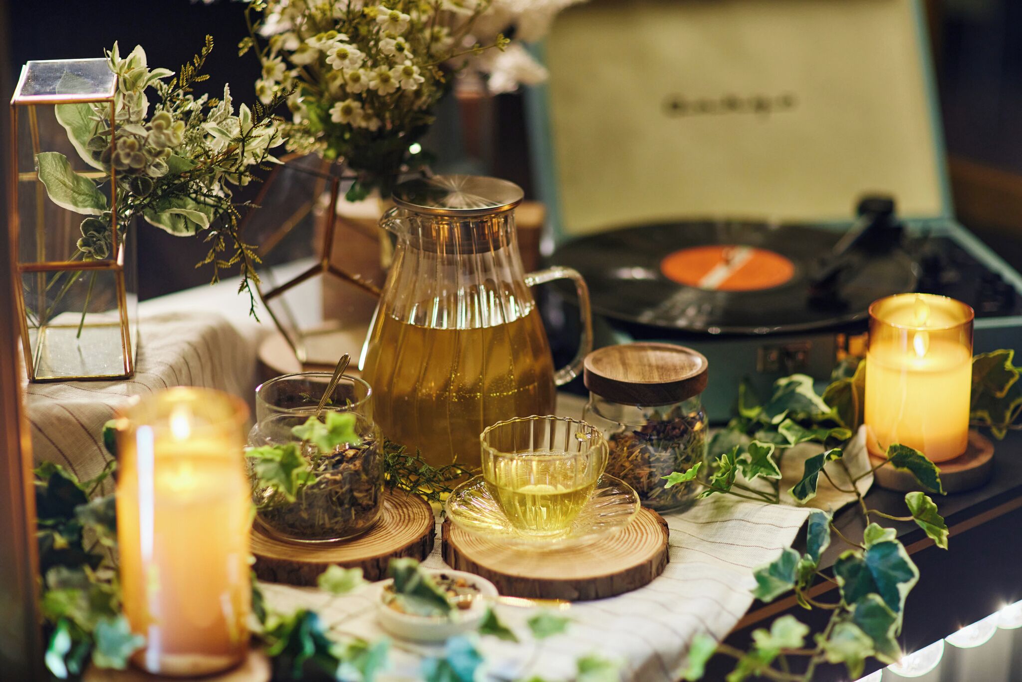 A table with a vinyl record player, a glass pitcher, candles, and decorative greenery.