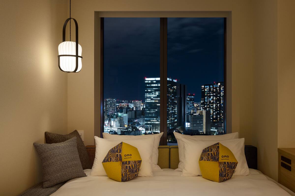 Une chambre d’hôtel avec vue sur la ville, un lit avec une literie blanche et deux oreillers à motifs géométriques.