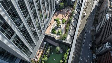 Um edifício alto com um jardim no terraço, incluindo áreas de estar e um pequeno lago.