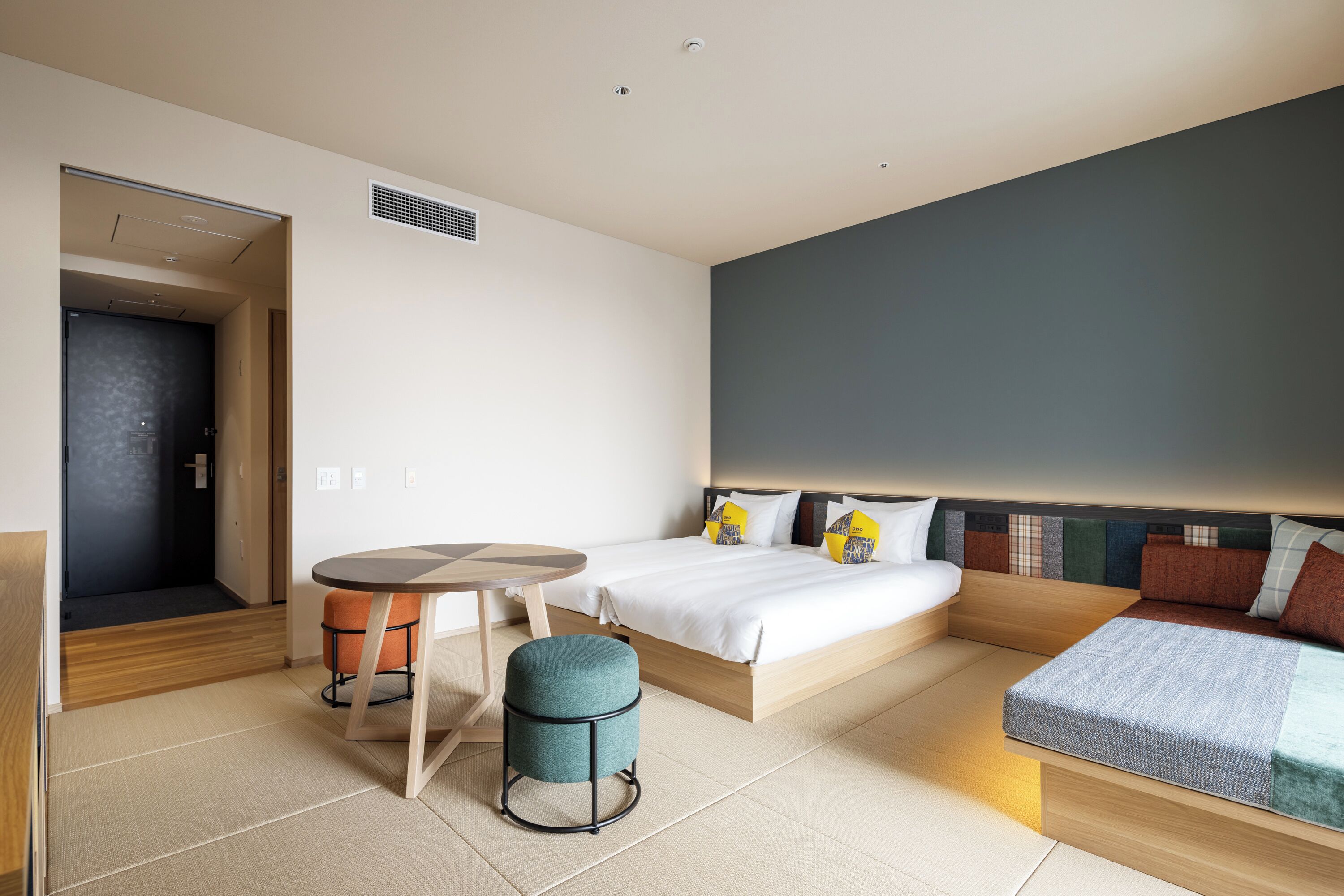 A modern hotel room with a bed, a sofa, a round table, and a small stool.