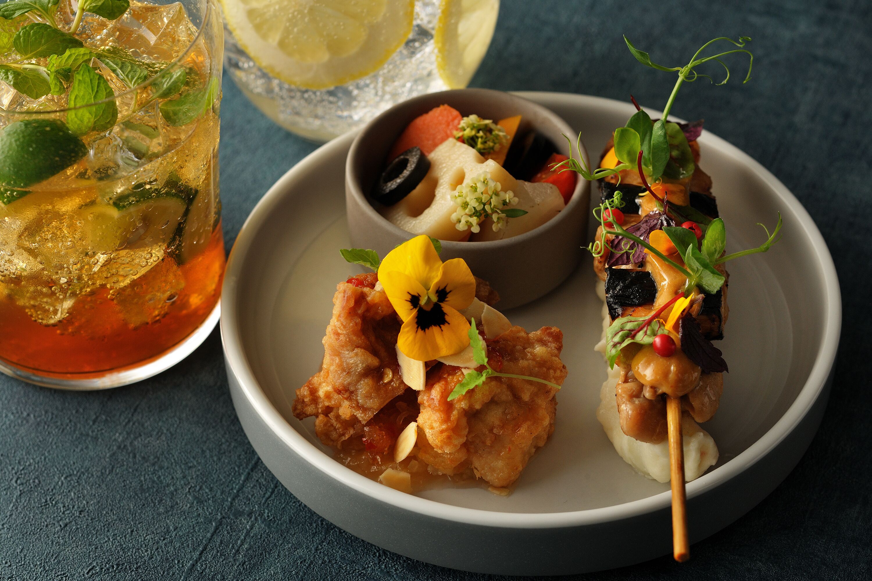 A plate of food with a drink and a lemon slice.
