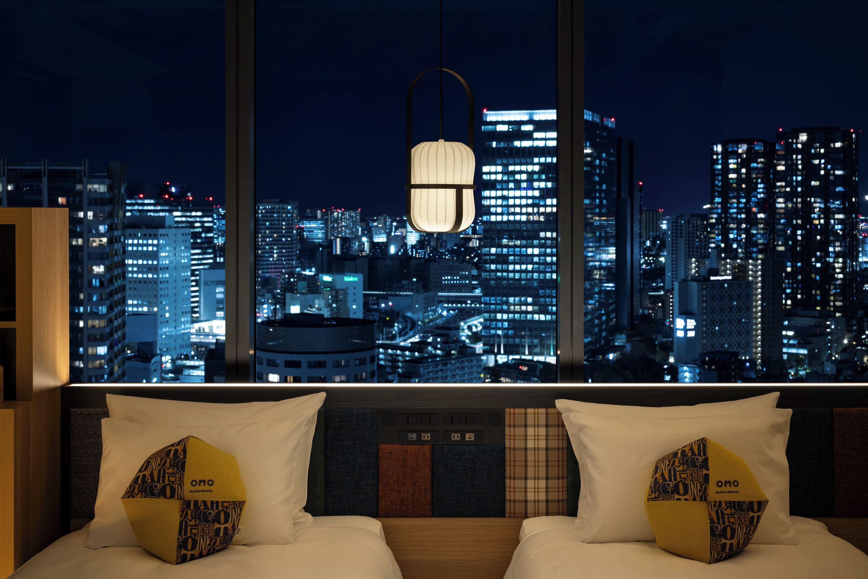 A hotel room with a city view, a hanging lamp, and patterned pillows.