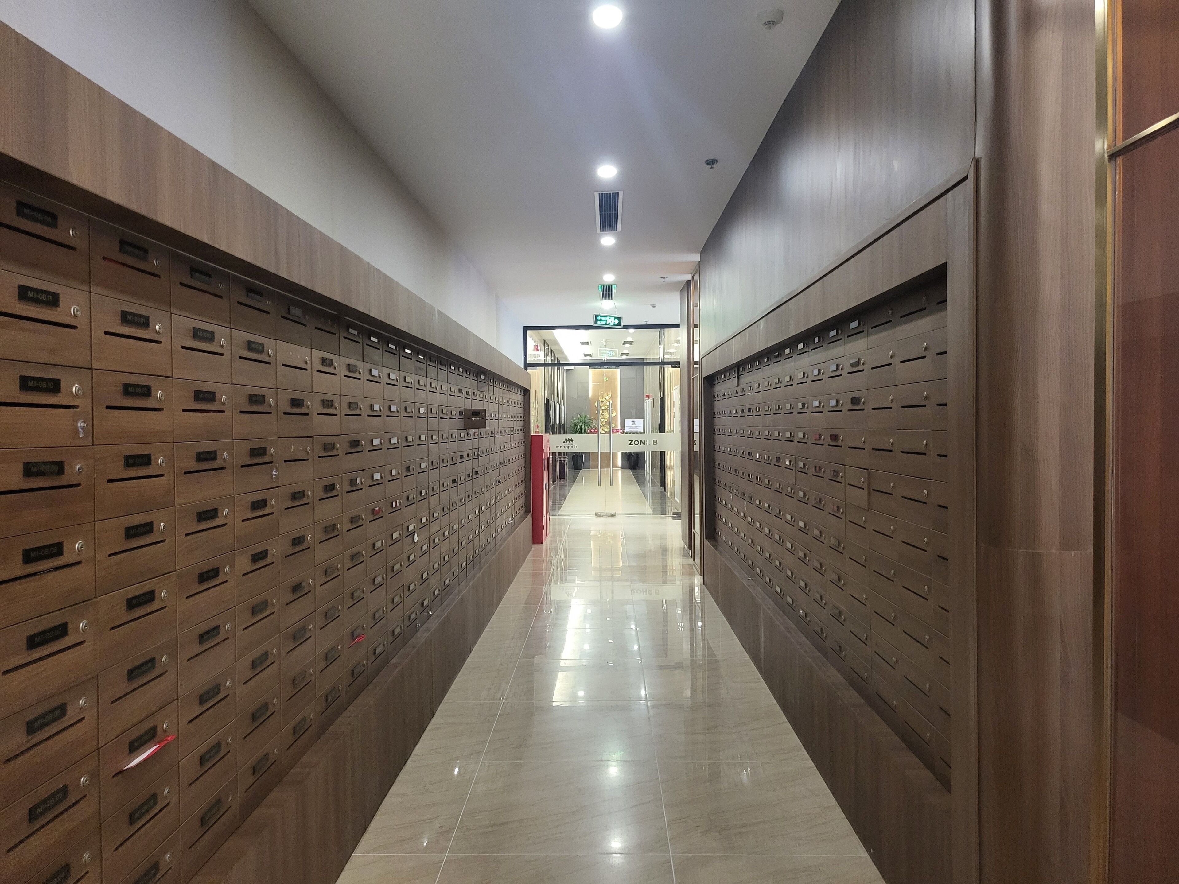 A hallway with rows of wooden lockers on both sides, leading to a reception area with a sign that reads "ZON B".