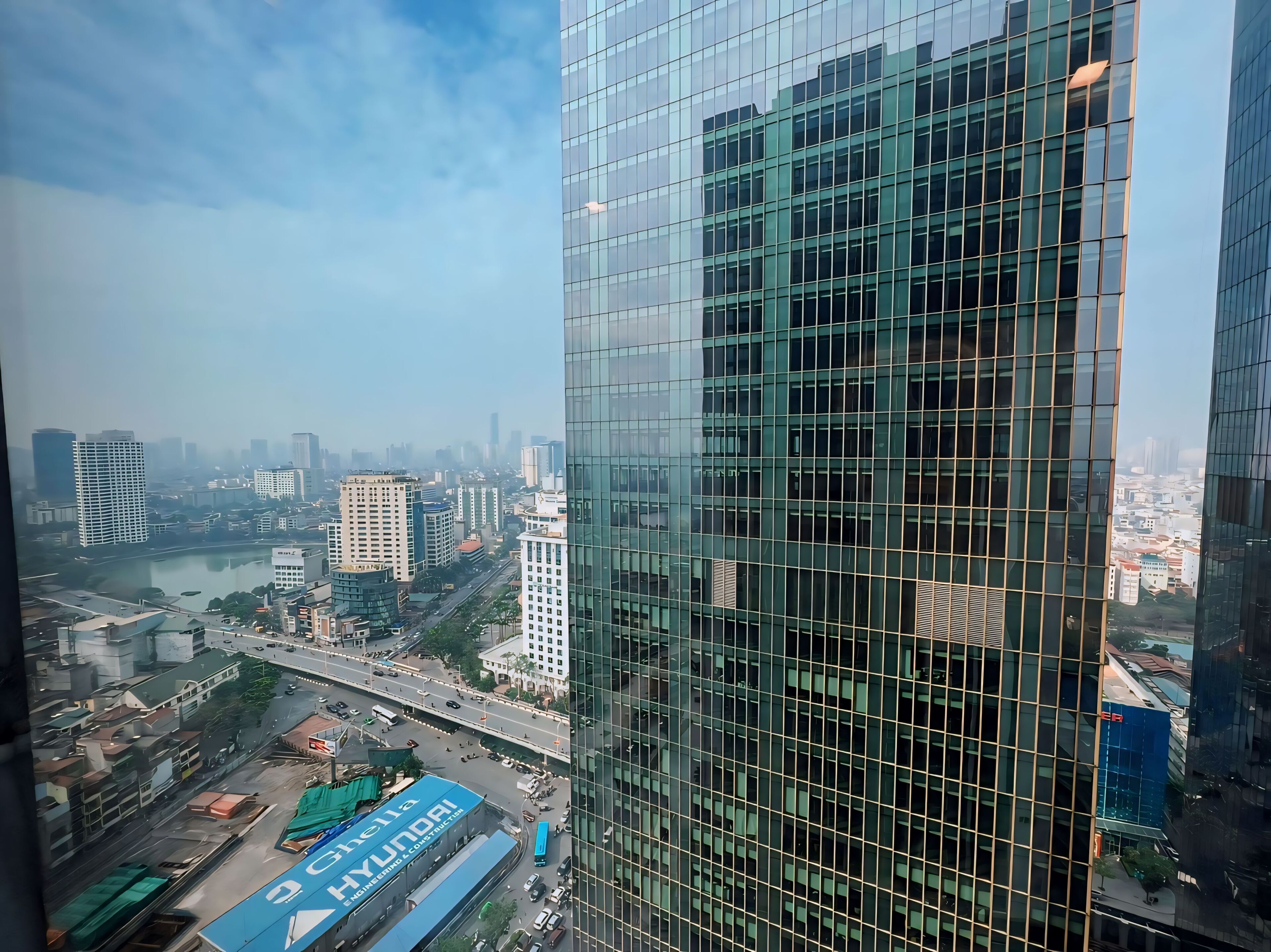 A high-rise building with a glass facade overlooking a cityscape with various buildings and a river.