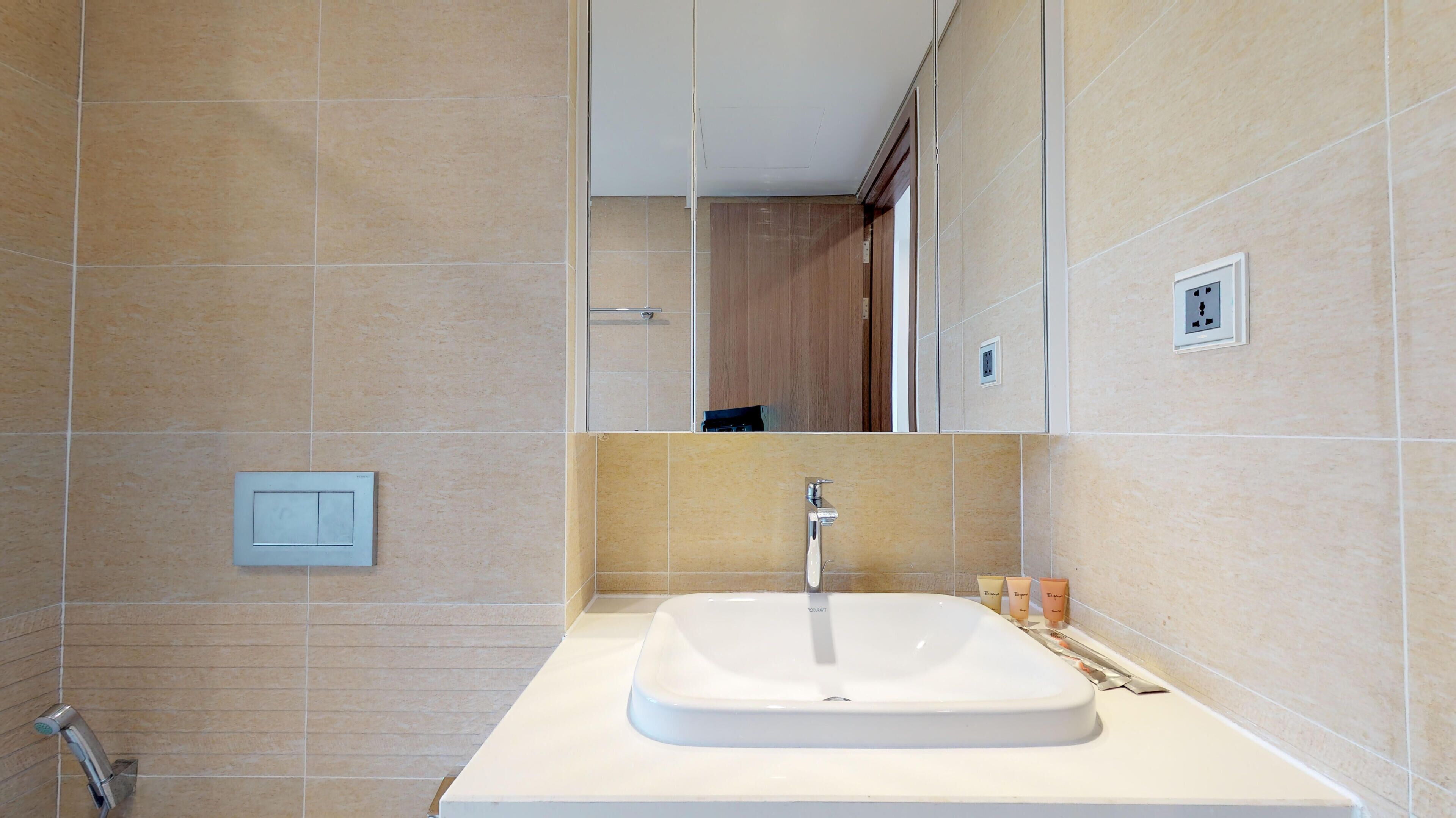 A modern bathroom with a white sink, a mirror above it, and beige tiled walls.