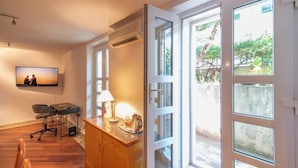 Una sala de estar moderna con televisor de pantalla plana, un mueble de madera, un escritorio con lámpara y un amplio ventanal corredero que da a un espacio exterior.