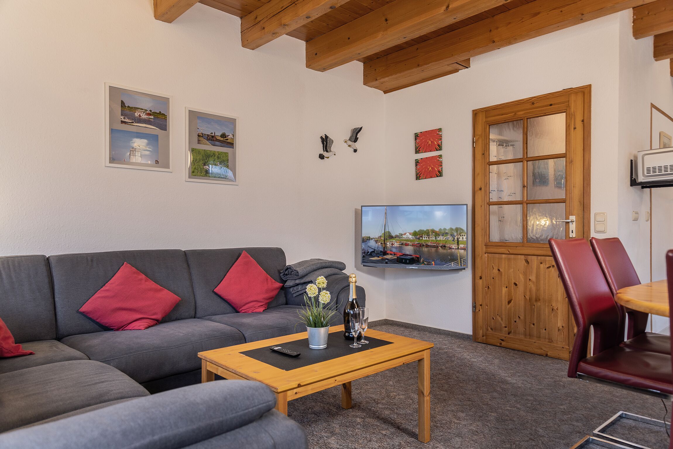 Un salon avec un canapé gris, des coussins rouges, une table basse en bois et un téléviseur fixé au mur.