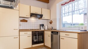 A kitchen with light-colored cabinets, a built-in oven, a dishwasher, and a window with a decorative valance.