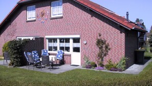 A red brick house with a sloped roof, a front porch with chairs, and a small garden area.