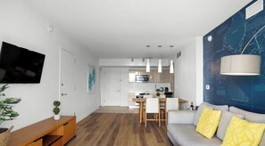 A modern living room with a grey sofa, yellow cushions, a wooden coffee table, and a TV on the wall. - Coastal Chic Spectacular Escape for Groups (Hallandale Beach)